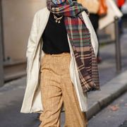 paris, france   january 28 a passerby wears a face mask, a green and brown checked fringed wool scarf, a black pullover, a golden necklace, a white wool long jacket, brown pants, on january 28, 2021 in paris, france photo by edward berthelotgetty images