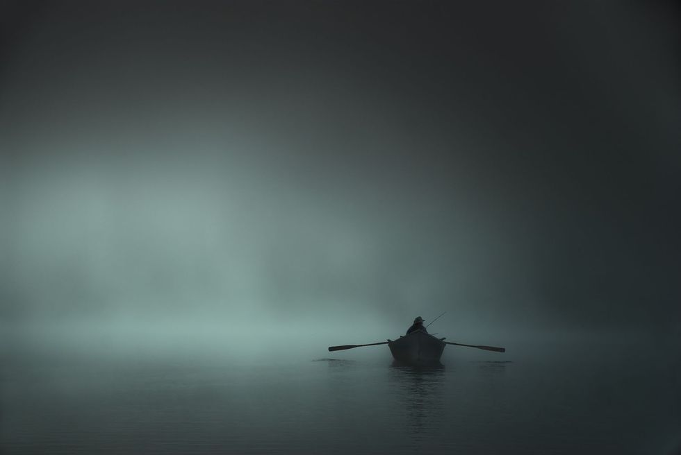 person fishing on a canoe in foggy weather