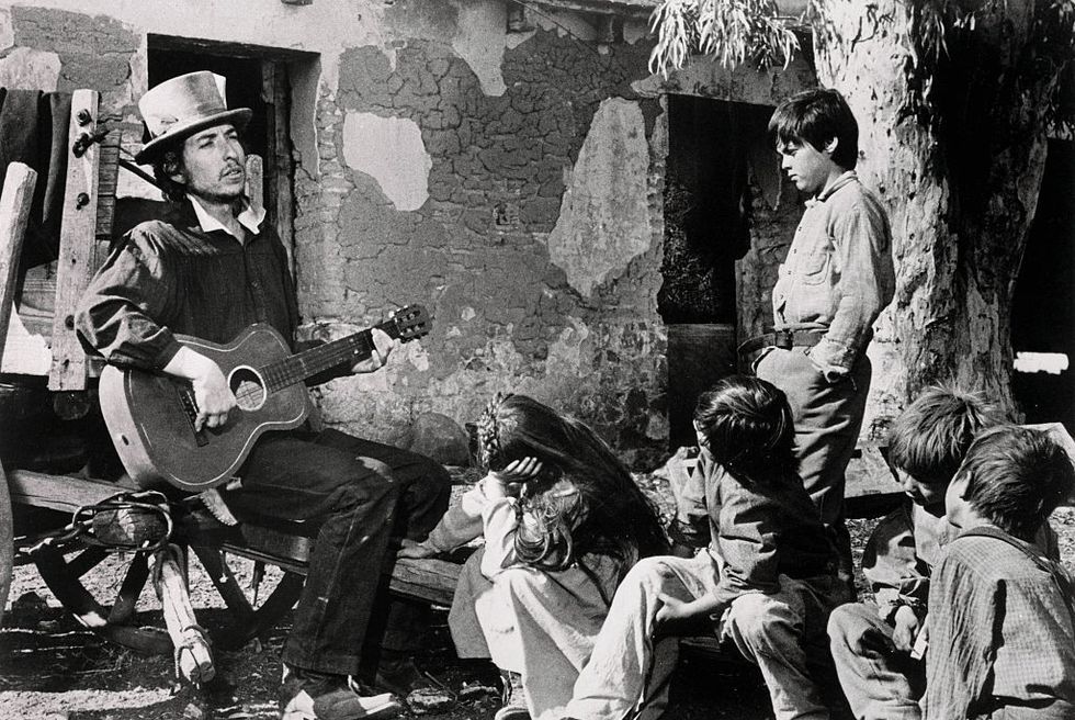 bob dylan plays guitar in a scene from pat garrett and billy the kid as children watch