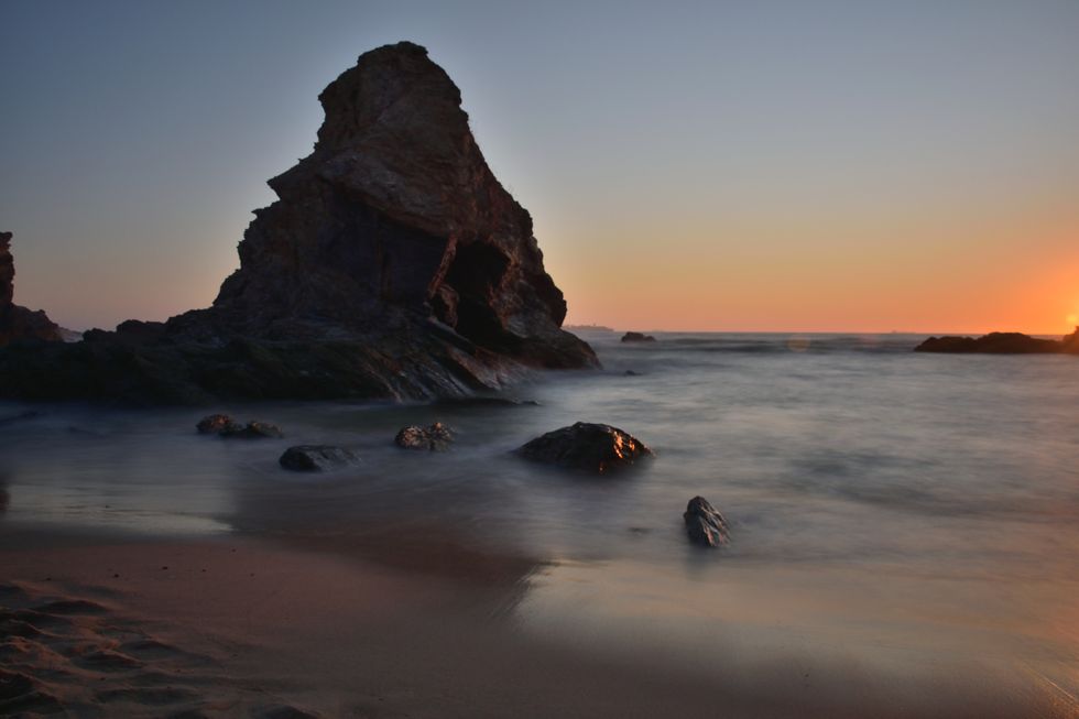 Uma bela vista do oceano contra o céu e formações rochosas durante o pôr do sol na Praia da Samoguera