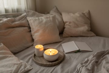 scented candles in ceramic bowls on linen bed with book at home