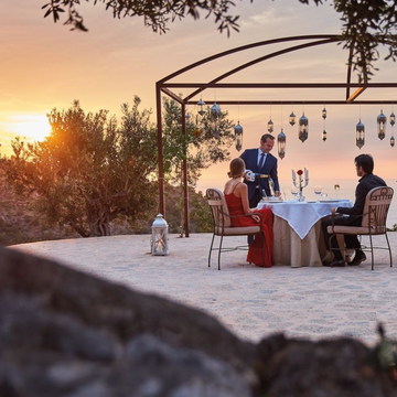 zonsondergang met olijfboom in mallorca met een romantisch diner met lantaarns en een vrouw in rode jurk en een man en ober