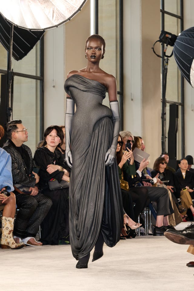 modelo desfilando com um vestido preto drapeado em um desfile de moda