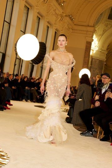 Model walking on runway in a detailed sheer gown at a fashion event