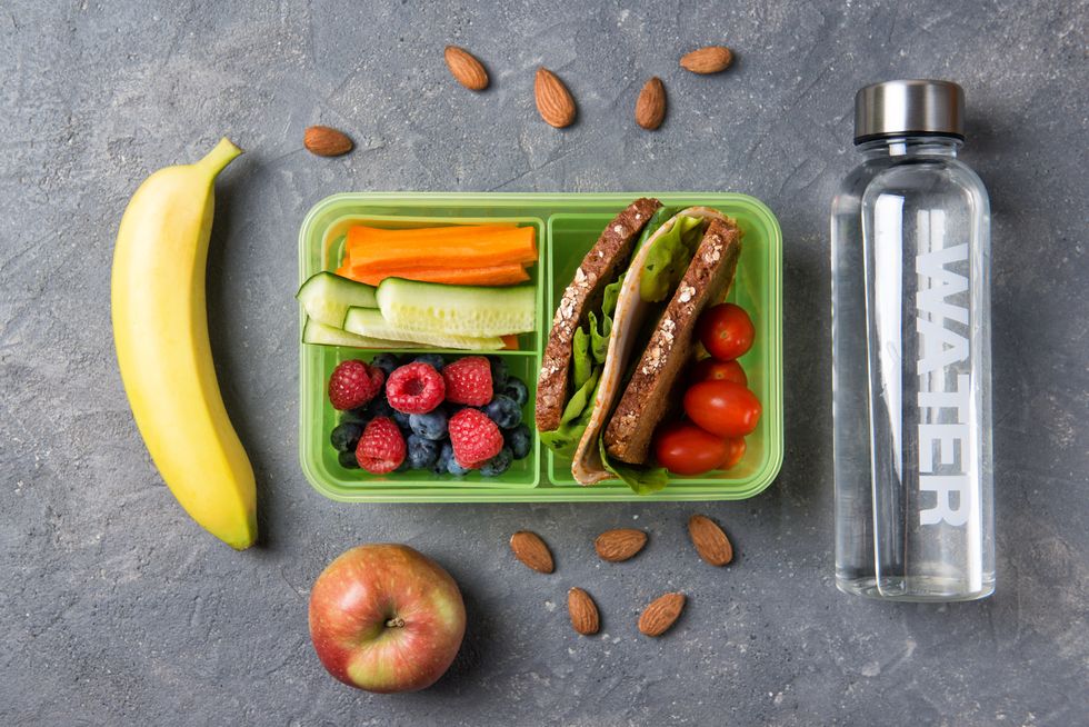 School lunch box with sandwich, vegetables, fruits and water on black background, healthy eating concept, top view