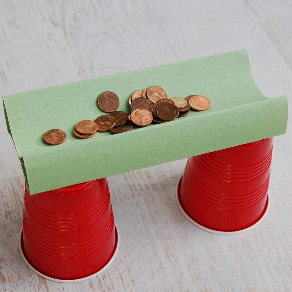 pennies sit on a construction paper bridge that spans two red solo cups in this science experiment for kids