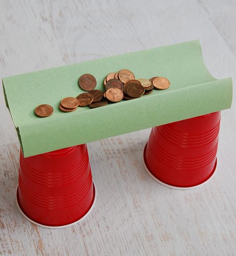 pennies sit on a construction paper bridge that spans two red solo cups in this science experiment for kids
