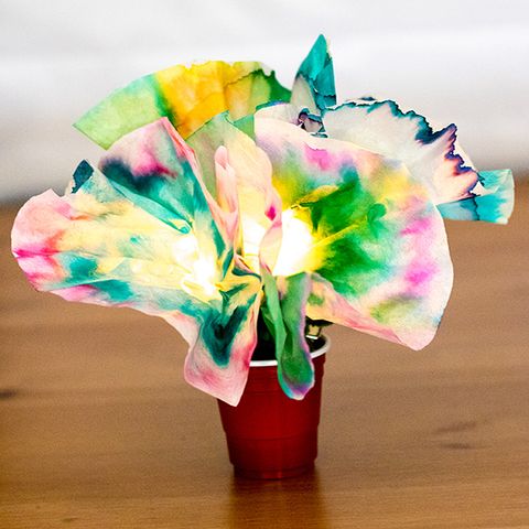 a coffee filter flower with an led in the center is decorated with swirls of color as part of this at home science experiment for kids