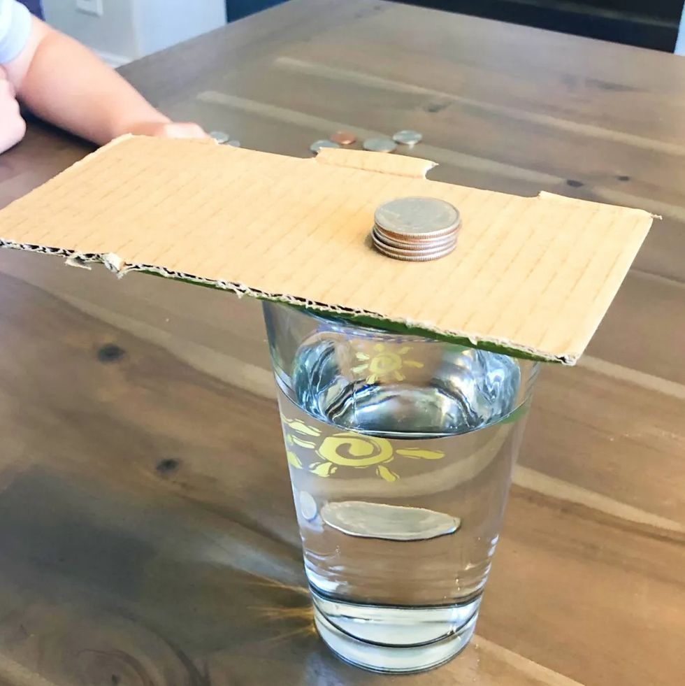 a stack of coins sits on a piece of cardboard on top of a glass of water as part of a science experiment for kids about inertia