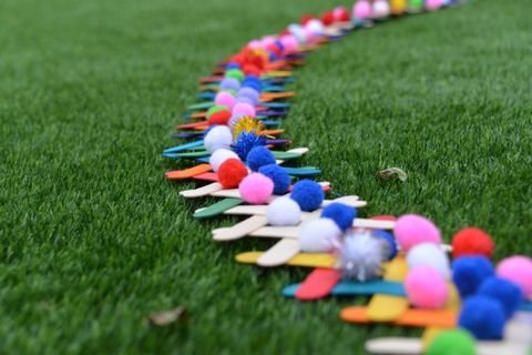 colored craft sticks with pom poms on top are lined up on grass as part of a science experiments for kids about chain reactions and potential and kinetic energy