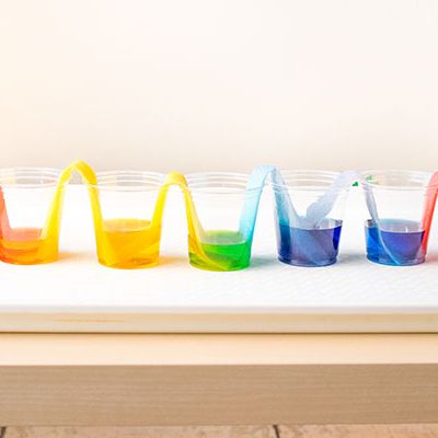 five cups with different colored liquid in them are connected by paper towel bridges as part of this at home science experiment for kids