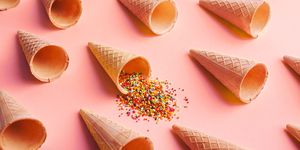 empty ice cream waffle cones and colorful sprinkles on pink background, side view