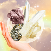 a hand holds up a fistful of different crystals in front of a rainbow sky