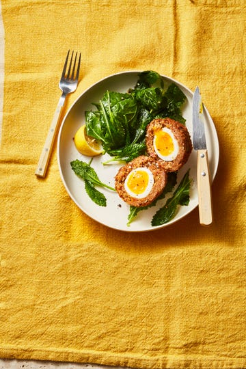 beef scotch eggs with leafy greens on a plate with knife and fork