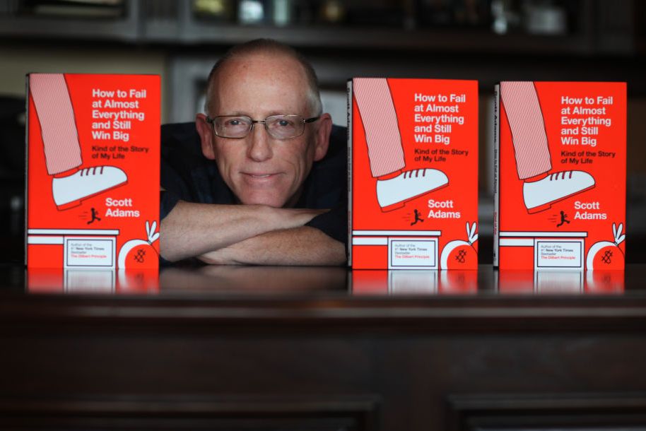 scott adams sitting at desk between copies of his book how to fail at everything and still win big