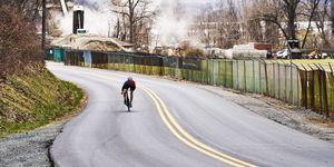 a person riding a bicycle on a road with a fence and trees