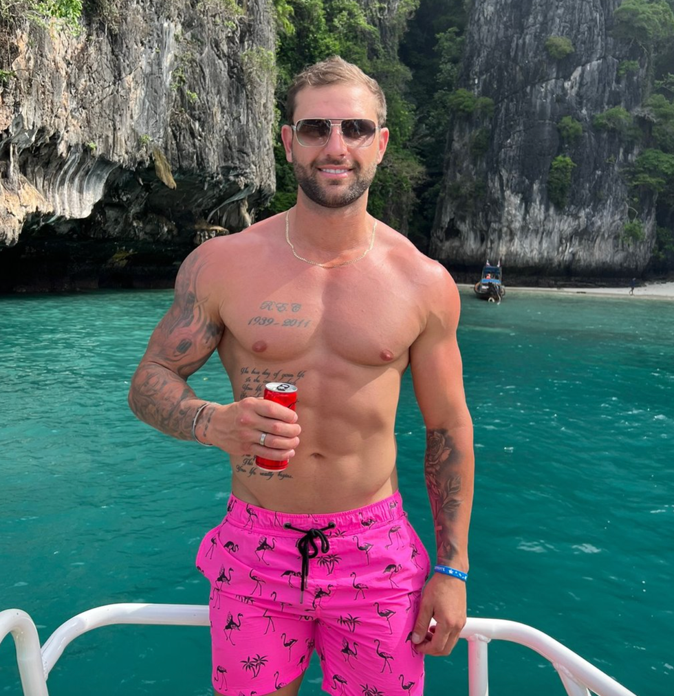 a shirtless man holding a drink on a boat with a tropical backdrop