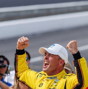indycar racing driver scott mclaughlin shouts with joy as he celebrates pole position at the indy 500, surrounded by team members, journalists and the firehawk bird mascot