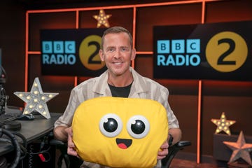 scott mills holding a yellow plush pillow with a smiling face in the bbc radio 2 studio for bbc bedtime stories