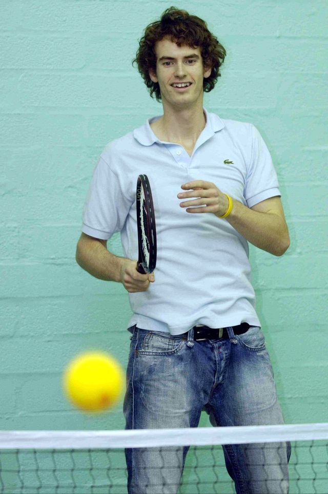 andrew murray watches a tennis ball soar over the net while holding a tennis racket, he wears a baby blue polo shirt and blue jeans