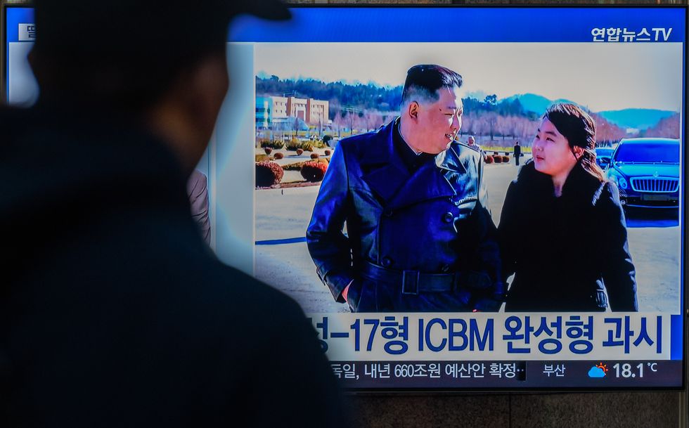a man watches a television screen with kim jong un and his daughter kim ju ae walking outside and talking