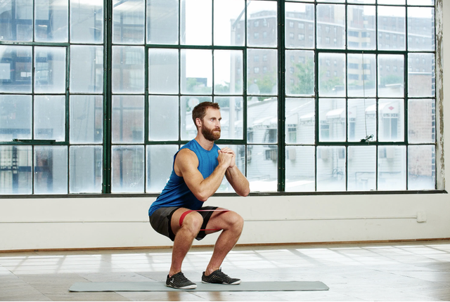 man doet squat met weerstandsband om zijn benen