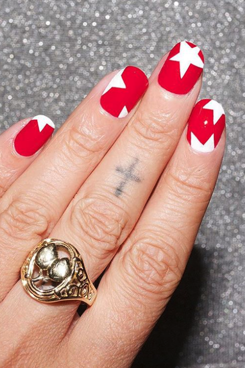 a manicure with a red base and white star designs, featuring a gold ring on a grey background
