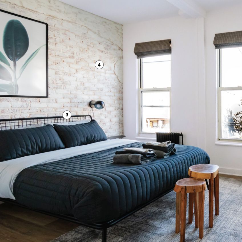 bedroom with white washed brick, black wire frame bed with blue comforter