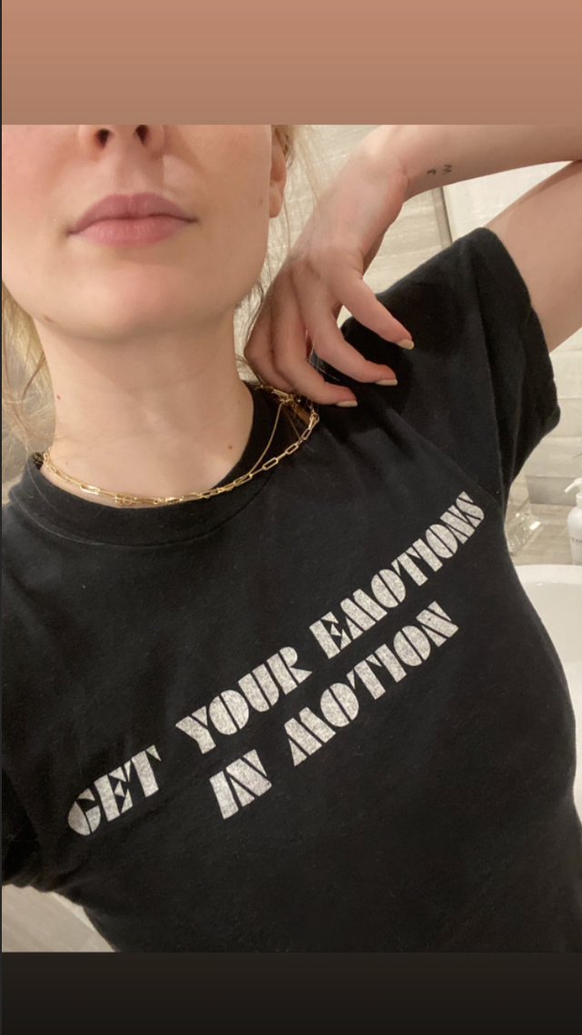 sophie turner posing in a black "get your emotions in motion" shirt, showing her wrist which now has both "j" and "w" tattooed on it