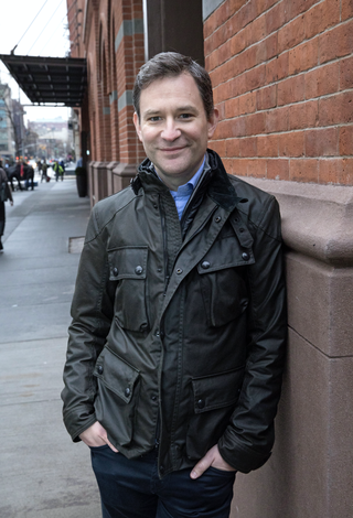 dan harris outdoors in a jacket, leaning against a wall