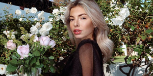 kit keenan posing in front of flowers and a blue background while wearing a black shirt