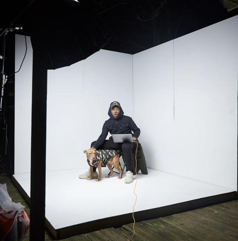 a man sits inside a white photo studio with a dog next to him