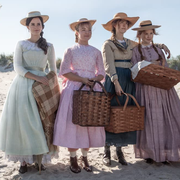 from left to right, emma watson, florence pugh, saoirse ronan, and eliza scanlen, four white actresses, in a still from little women where they are standing on a beach in 1800s clothing