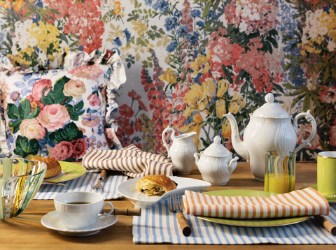 a table setting with striped napkins, white teapot and other homeware and a floral backdrop