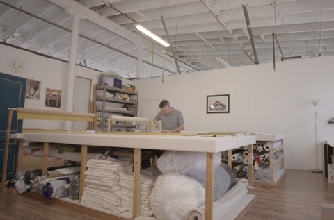 joseph boisne stands at a table in his workshop, crafting an upholstered door