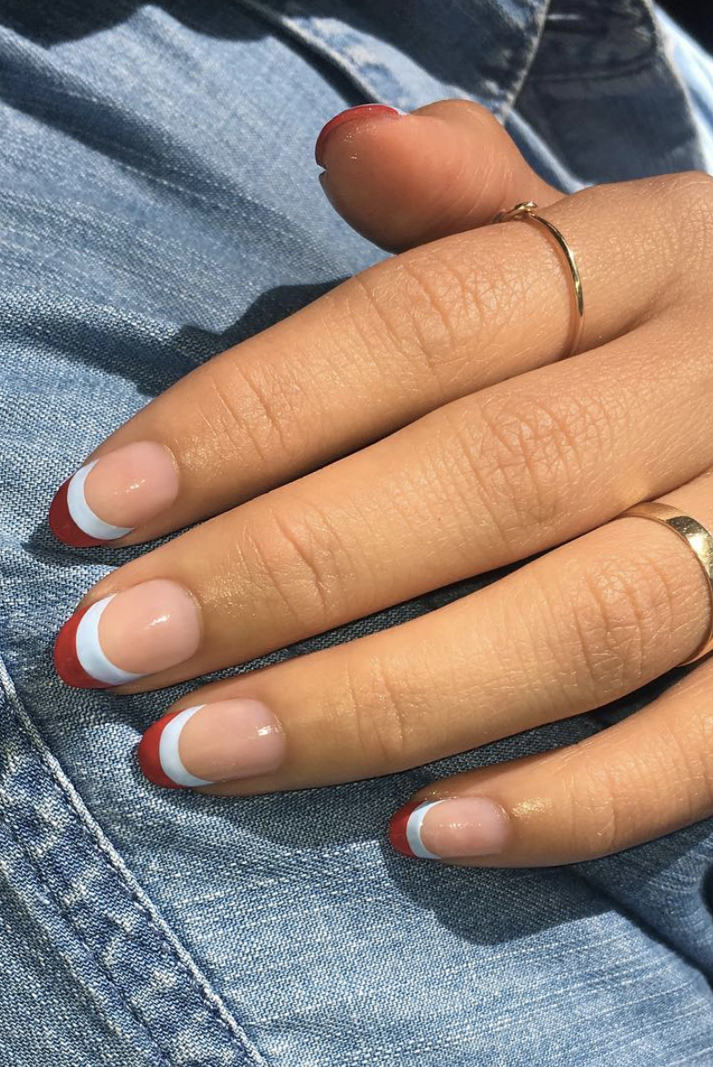 a hand with a red and white double french manicure and gold rings is placed on a denim background