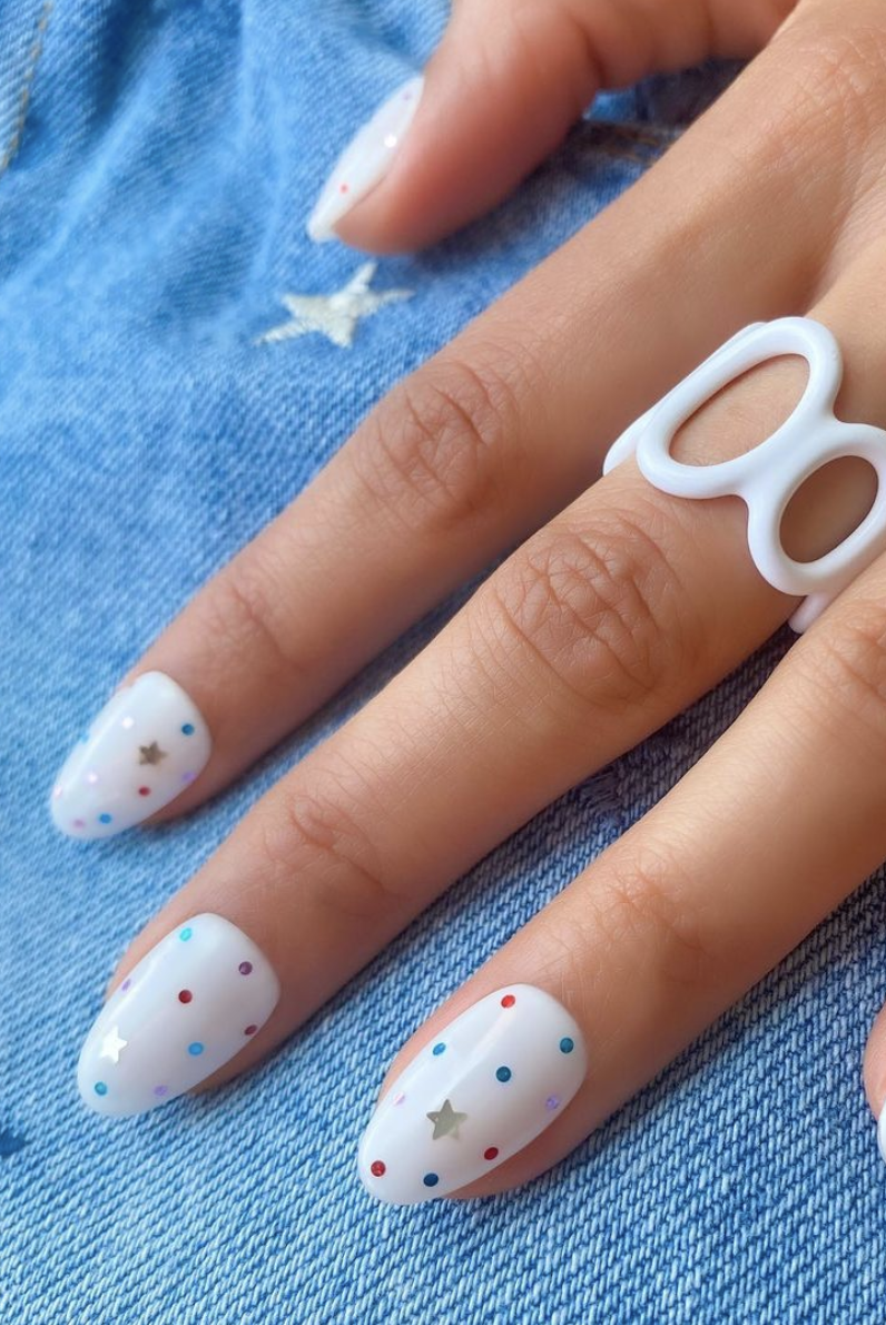 a white manicure with colorful star and polka dot designs on a denim background