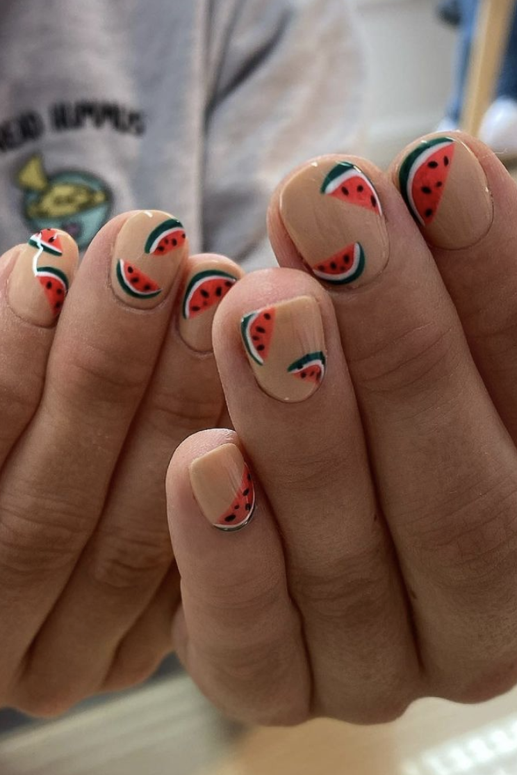a nude manicure, featuring a unique red, black, white, and green watermelon design on each fingernail