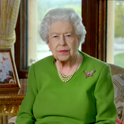 This is an image queen elizabeth wears green dress, pearls, and butterfly brooch while sitting next to a photo of prince philip among butterflies