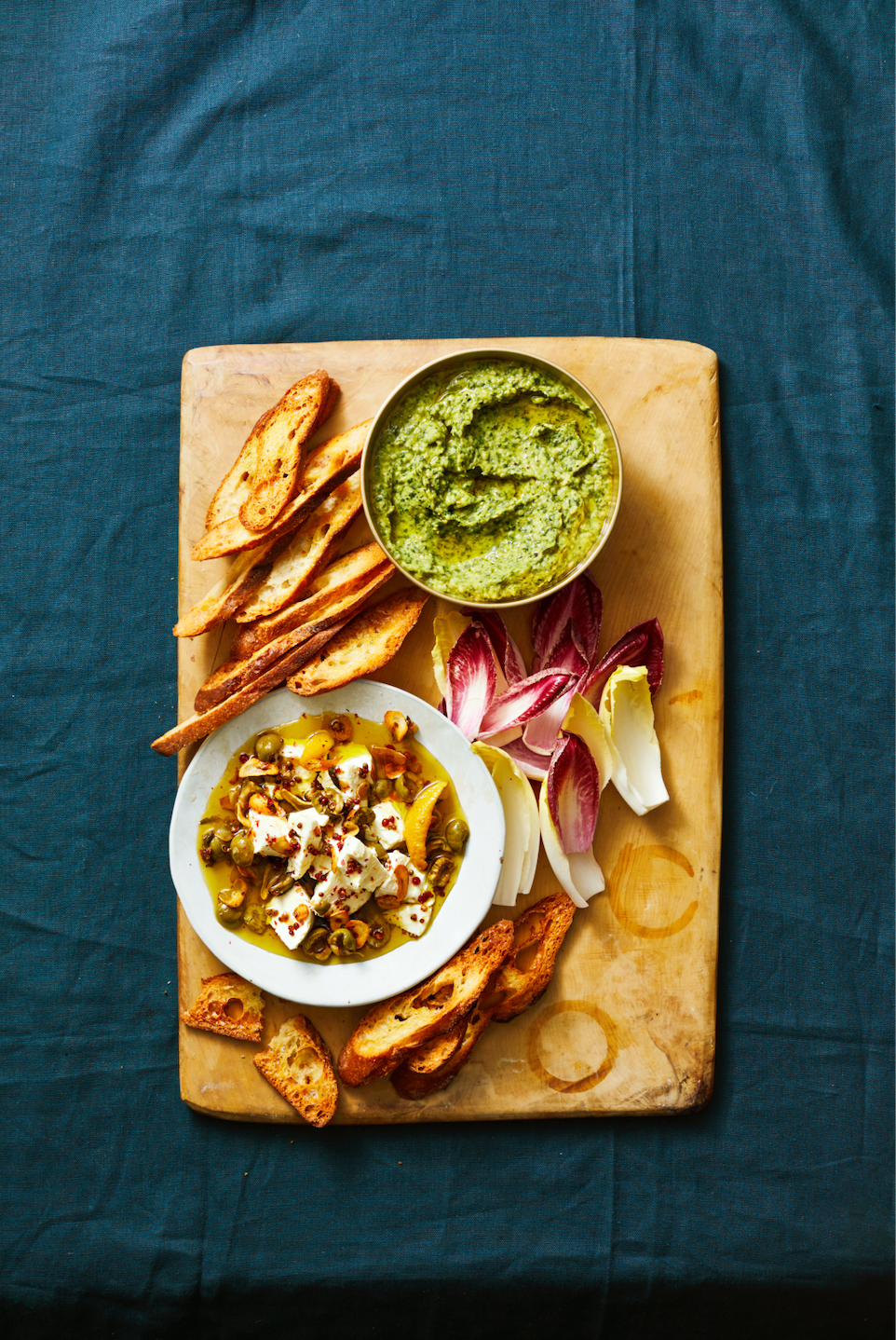 a green herby log of goat cheese on a white plate with slices of crusty toast on the side