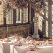 a table set with a pink tablecloth with light pink dishes and candles in an old italian villa next to a bust