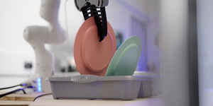 dyson household chore robot gripping a pink plate with a green plate resting in a drying rack on the right side
