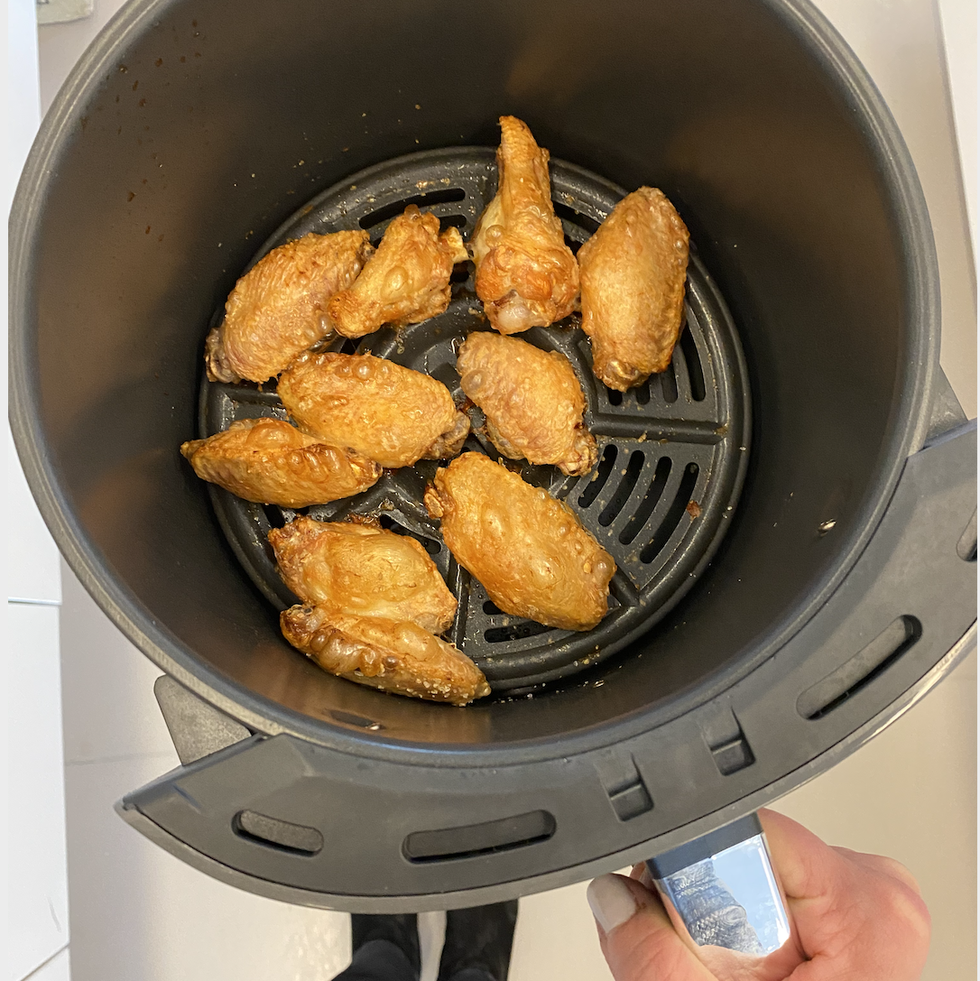 overhead shot of hand holding the ninja air fryer max xl cooking basket which contains golden brown chicken wings
