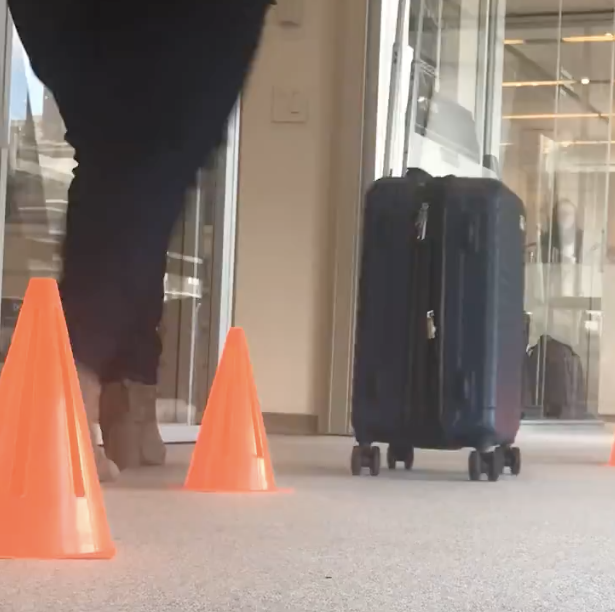 someone rolling a carryon suitcase through a cone obstacle course at good housekeeping institute