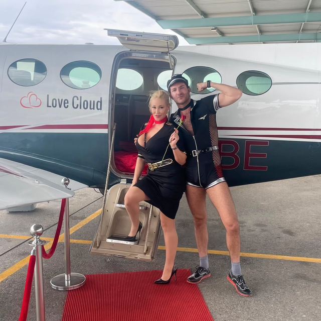 a couple in sexy pilot and flight attendant costumes pose outside a private jet