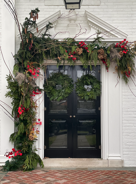 a christmas door with two wreaths and a large garland arch