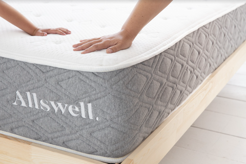 hands pushing down on the corner of an allswell luxe hybrid mattress