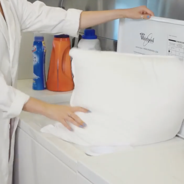 hands putting a pillow in a washing machine to show how good housekeeping tests pillows