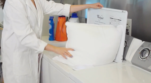 hands putting a pillow in a washing machine to show how good housekeeping tests pillows