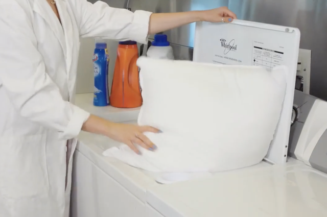 hands putting a pillow in a washing machine to show how good housekeeping tests pillows